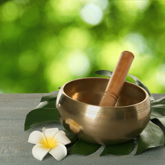 Golden singing bowl, mallet, leaf and flower on grey wooden table outdoors