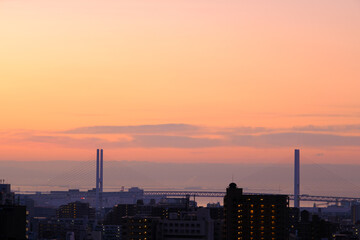 Fototapeta na wymiar 早朝、日が昇りあたりはオレンジ色に染まる。雲に隠れていた太陽が顔を出す。大阪湾の先に和泉山脈・紀伊山地の稜線が見える。