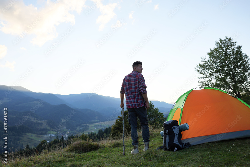 Poster Tourist with backpack and sleeping pad near camping tent in mountains