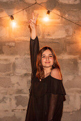 A teenage girl near the wall with flashlights in black dress. The girl has a positive cheerful mood.