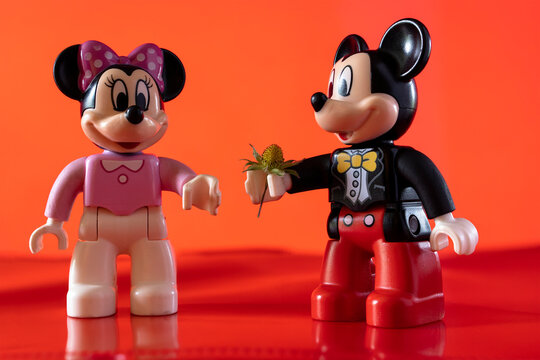 New York, USA - May 25, 2021: A close up shot of a miniature famous Disney character "Mickey Mouse" handing over a flower to "Minnie Mouse" against a red background