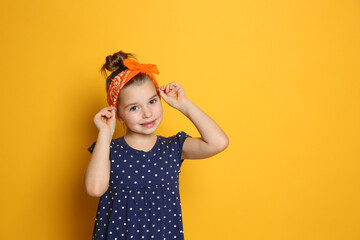 Cute little girl wearing stylish bandana on orange background, space for text