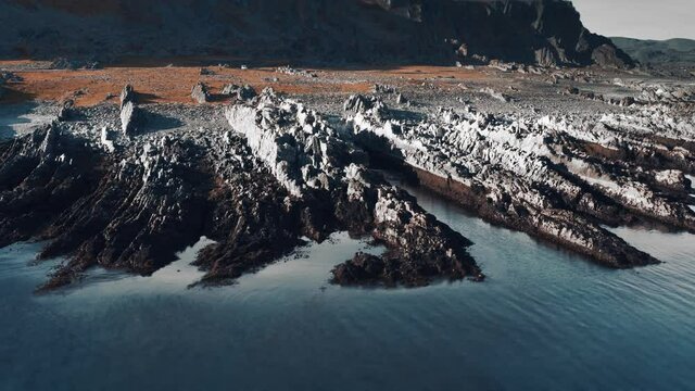 Bird's eye view of the harsh coastal landscape of the Varanger peninsula. Dark jagged cliffs protrude far into the sea. Narrow road snaking along the shore. Pan right