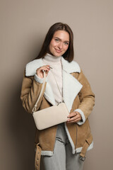Fashionable young woman with stylish bag on beige background