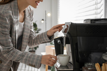 Fototapeta na wymiar Young woman preparing fresh aromatic coffee with modern machine in office, closeup