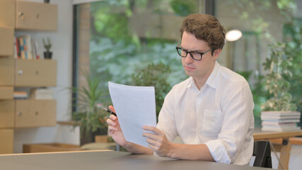 Young Man Reading Documents while Sitting in Modern Office