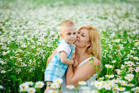 A plump woman and a small one-year-old boy in a field of daisies. A mother has fun with her son in a blooming field of chamomile.
