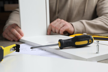 Man assembling wooden furniture at table, focus on screwdriver