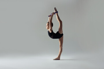 Cute little gymnast with rope doing standing split on white background