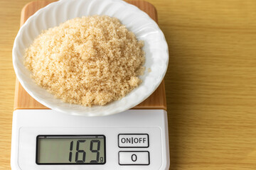 デジタルキッチンスケールで茶色い砂糖（粗糖）を量るイメージ