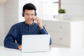 Young asian businessman working on laptop computer wearing headphone at home, business man wearing headset for video conference, communication and education, male study and learning for e-learning. - Powered by Adobe