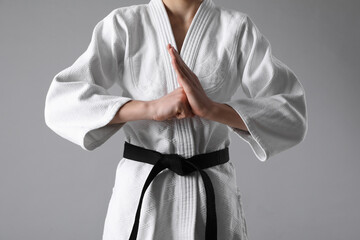 Martial arts master in keikogi with black belt on grey background, closeup