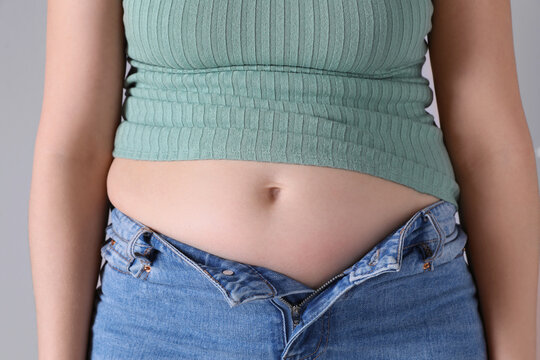 Woman wearing tight clothes on light grey background, closeup. Overweight problem