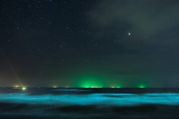Stars in the night sky and green lights from a fishing boat at sea.