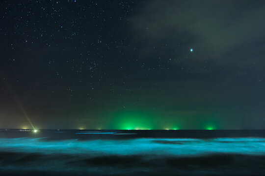 Stars in the night sky and green lights from a fishing boat at sea. © Kittipan