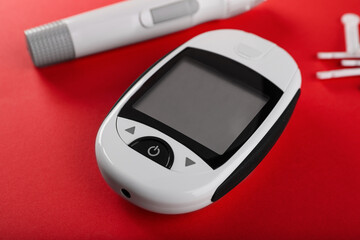 Digital glucometer, lancets and pen on red background. Diabetes control