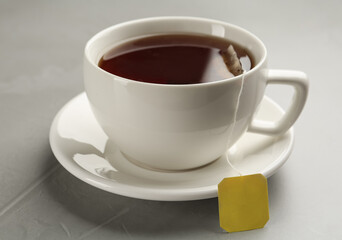 Tea bag in ceramic cup of hot water on grey table