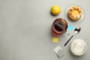 Flat lay composition with tea bag in ceramic cup of hot water and dessert on grey table. Space for...
