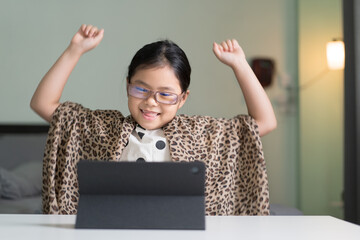 Asian child sitting smile raising hands and dancing on computer tablet or kid girl student wearing...