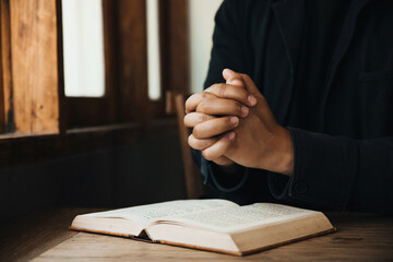 Handsome man hands are praying for God's blessings on an open bible with window light Pray in the Morning. begging for forgiveness and believing in goodness.