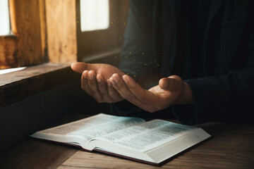 Handsome man hands are praying for God's blessings on an open bible with window light Pray in the Morning. Power of hope or love and devotion.