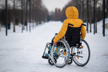 Caucasian woman with disabilities rides on a chair in the park in winter. Back view of a girl on a walk in a wheelchair. 
