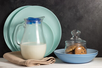 A jug of milk and a jar of oatmeal cookies on a background of clean plates.