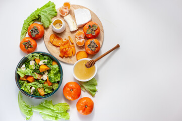 Light sweet and sour salad with persimmon, tangerines and cheese. Winter vitamin salad and ingredients on a White table. Diet food. Vegan breakfast or lunch. View from above.