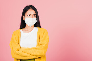 Asian beautiful young woman wearing medical mask protection for prevent infection coronavirus, COVID-19 she crossed arms, studio shot isolated on pink background copy space medical health care concept