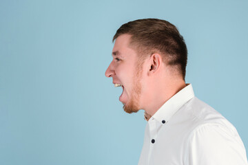 A bearded man shouts with his mouth open portrait in profile on a blue background