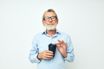 Senior grey-haired man gestures with his hands a glass of drink light background
