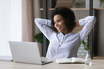 Relaxed happy young african american business woman employee worker enjoying carefree break time after hard working day in modern office, resting finishing online project or meeting deadline.