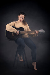 Fototapeta na wymiar Young woman playing acoustic guitar with smoke and black background