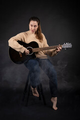 Young woman playing acoustic guitar with smoke and black background