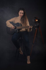 Fototapeta na wymiar Young woman playing acoustic guitar with smoke and black background