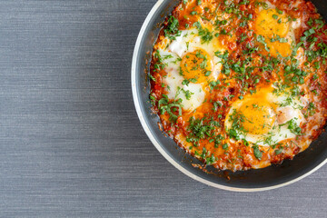 Shakshuka a traditional dish of eggs tomatoes and peppers with the addition of aromatic spices and fresh parsley in a pan, close up.