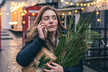 A young woman with a Christmas tree and a gift box talking on the phone.