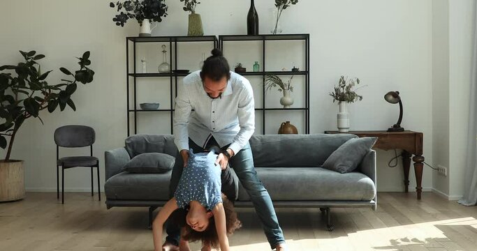 African father play with little adorable child, whirls his flexible daughter, 10s active girl perform handstand enjoy playtime with dad at modern home. Sportive family games, lifestyle and fun concept