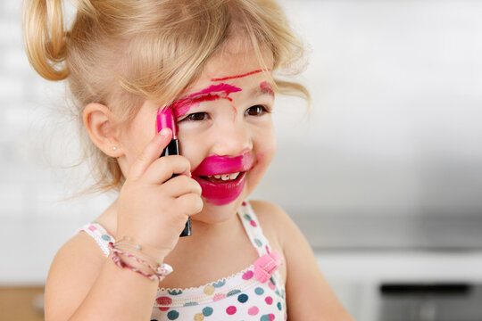 Close up of smiling toddler girl applying lipstick messily