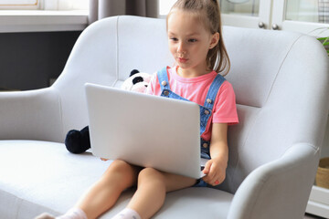 Distance learning. Cheerful little girl using laptop computer studying through online e-learning...