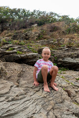 Child boy sitting on rocks by the ocean. Adventure by the sea