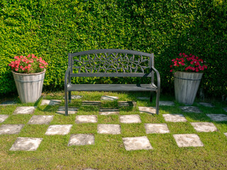 Empty black iron bench decorated between two flower pots on the green grass, the checkered pattern...