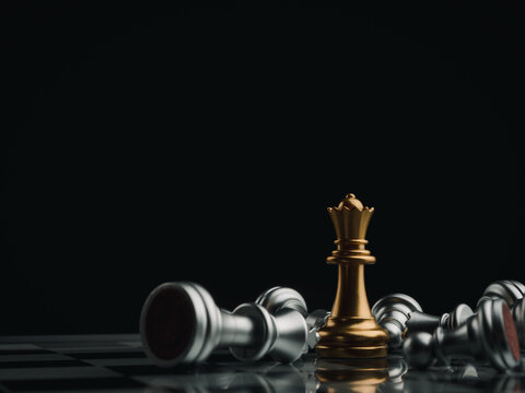 The gold queen chess piece standing with falling silver pawn chess pieces on chessboard on dark background with copy space. Leadership, winner, competition, and business strategy concept.