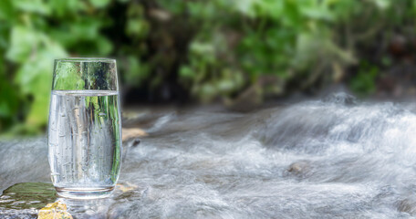 a glass of clean transparent drinking water in a transparent glass on a stone in a green forest near a stream or mountain spring. healthy food and diet, beautiful background copy space