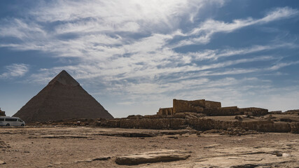 The Great Egyptian pyramid of Chephren against a background of blue sky and clouds. The ruins of an...
