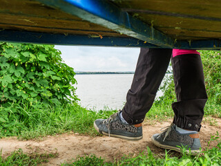 The girl sits by the lake, wears on her feet sneakers. Female legs