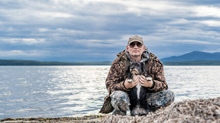 Happy pensioner sits with dogs on the seashore. Satisfied with rest.