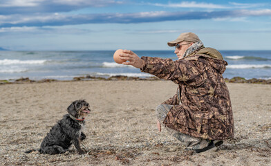 Happy man playing ball with dog on the seashore