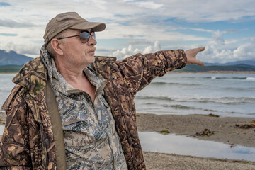 Portrait of a pensive elderly man on the seashore, pointing to the distance