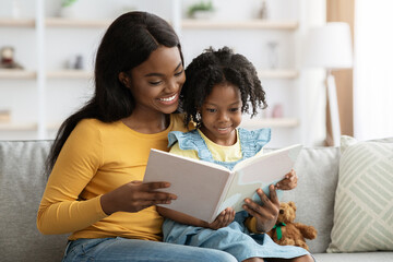Loving black mom reading book to her cute little daughter at home